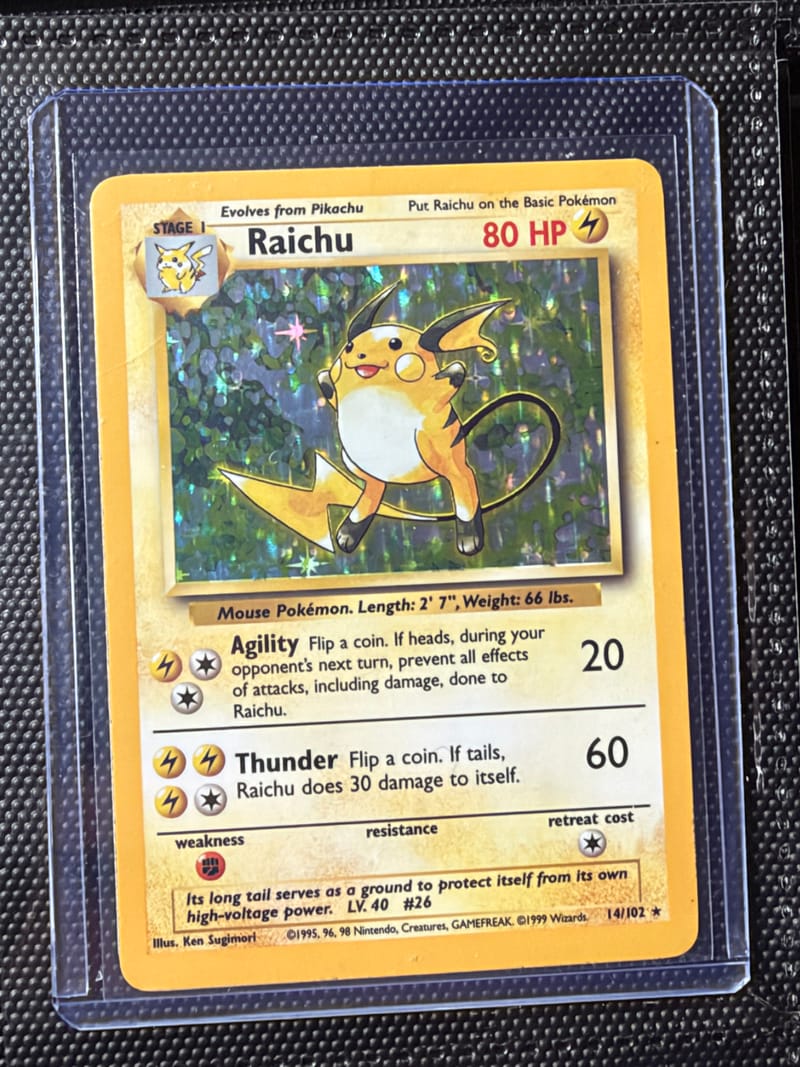 A Base Set Raichu 14/102 holo in a toploader, with white along the edges and wear on the surface